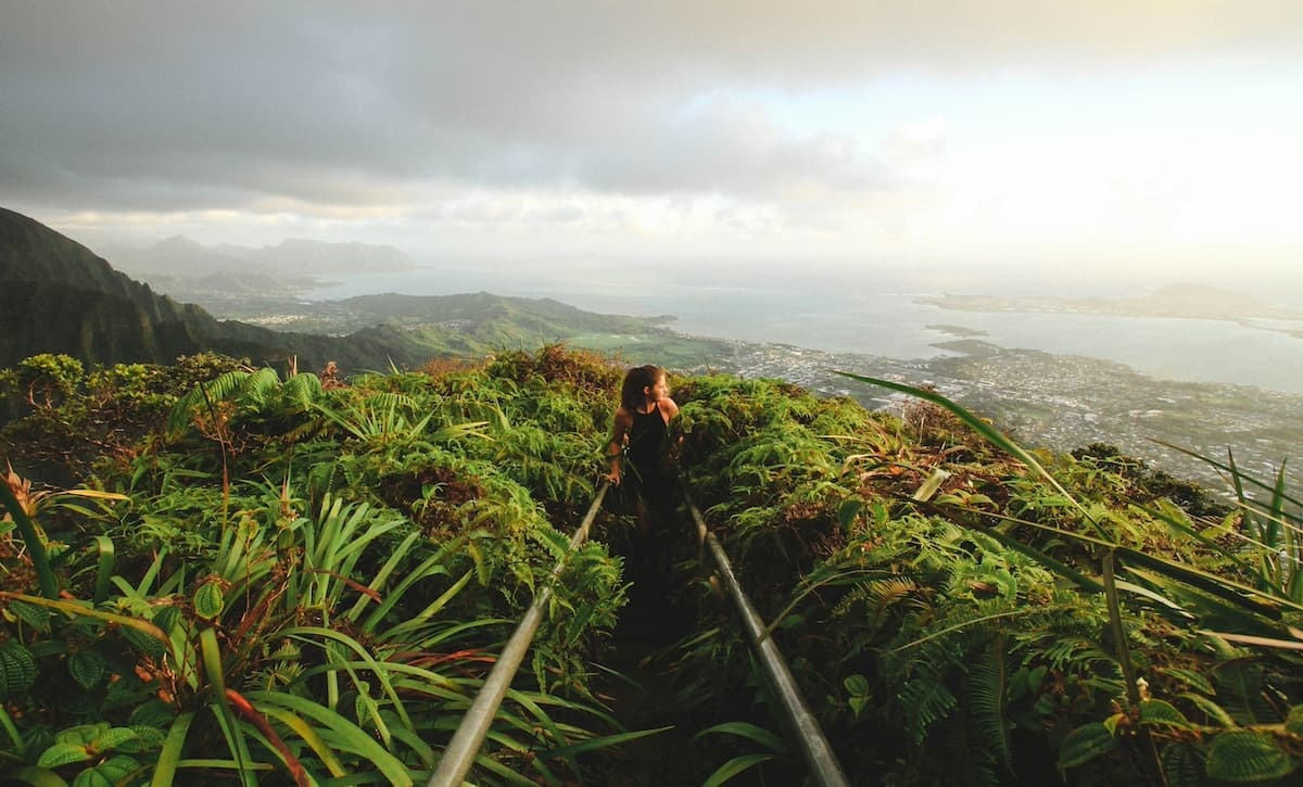 A woman hiking on a jungle trail on Oʻahu with the ocean in the background