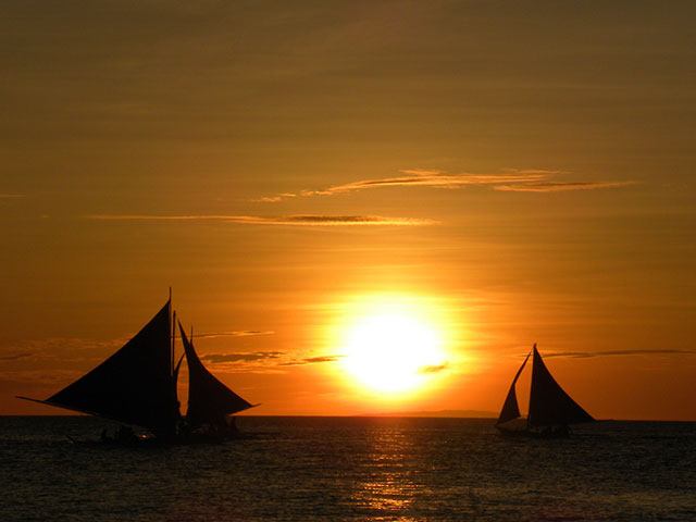 Two sailboats silhouetted against an orange sunset