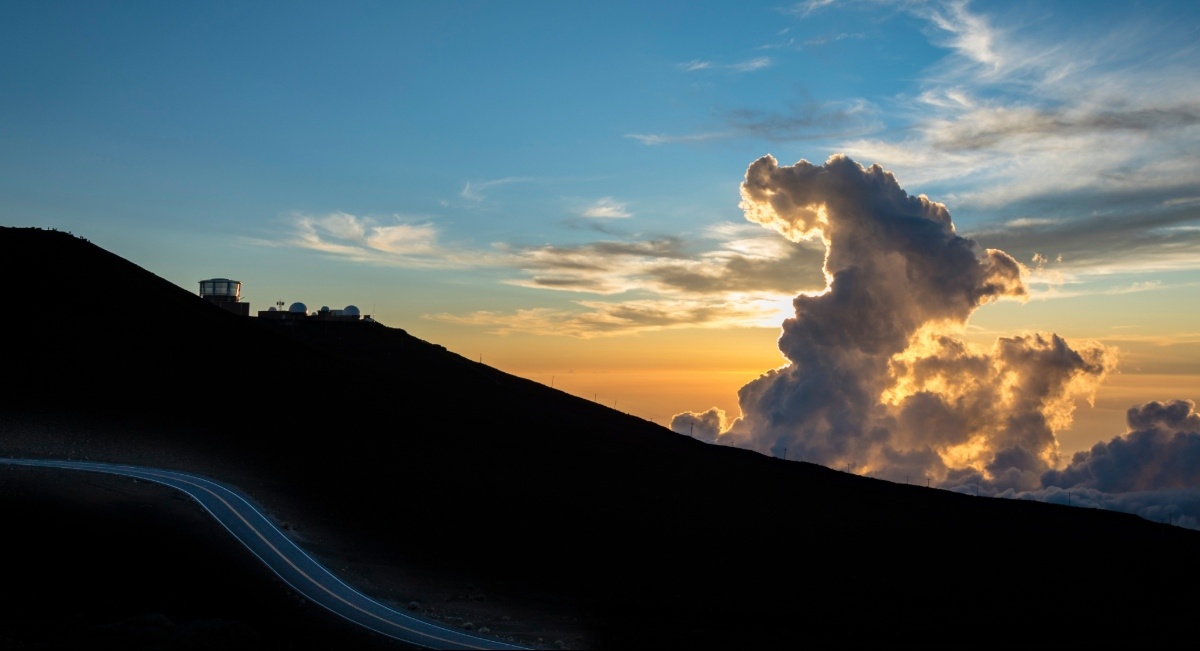 Pre-dawn sky above the Haleakalā summit with golden clouds and a winding road on the mountain slope, Haleakalā National Park, Maui