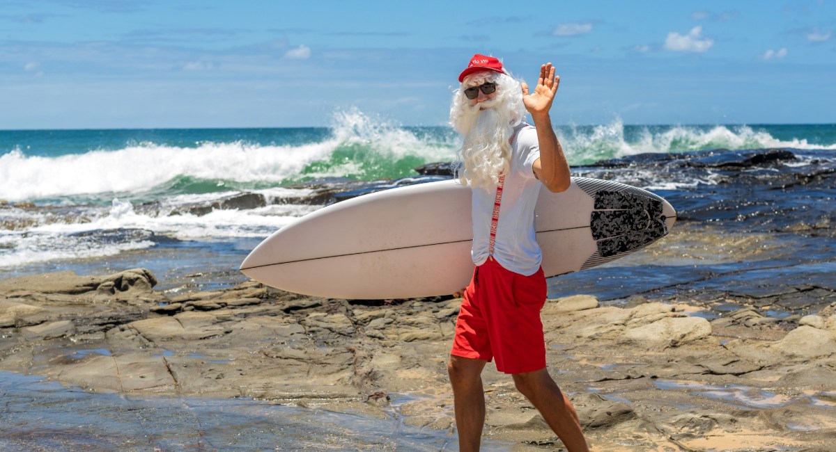 Santa Claus with surfboard on Maui Hawaiʻi beach celebrating a tropical Christmas holiday
